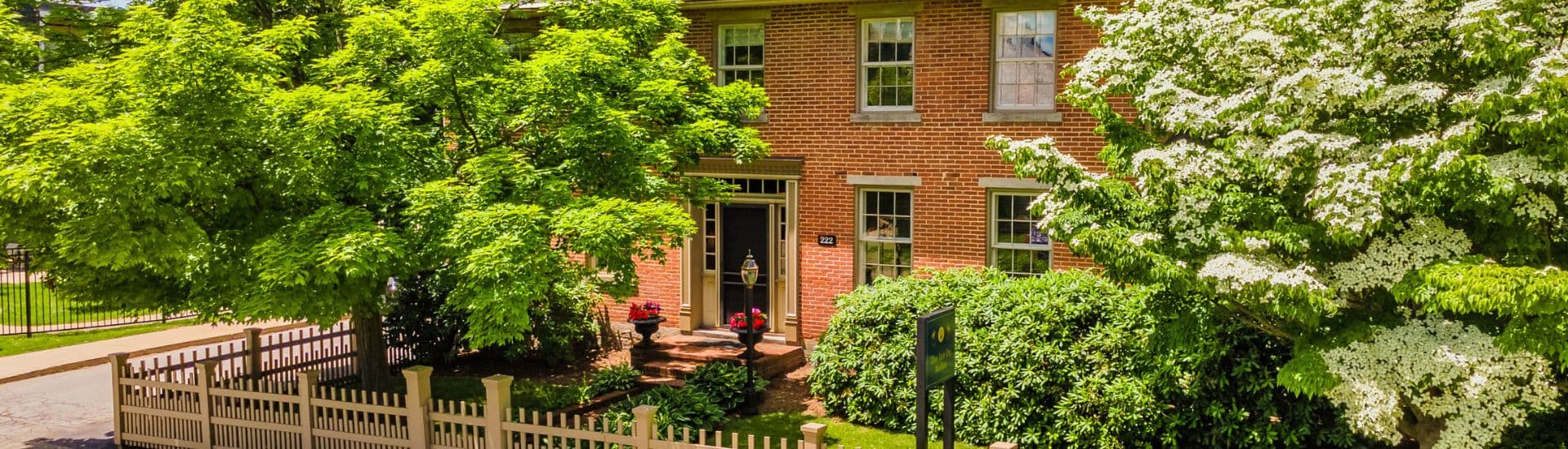 A brick house surrounded by lush green trees and colorful flowers.