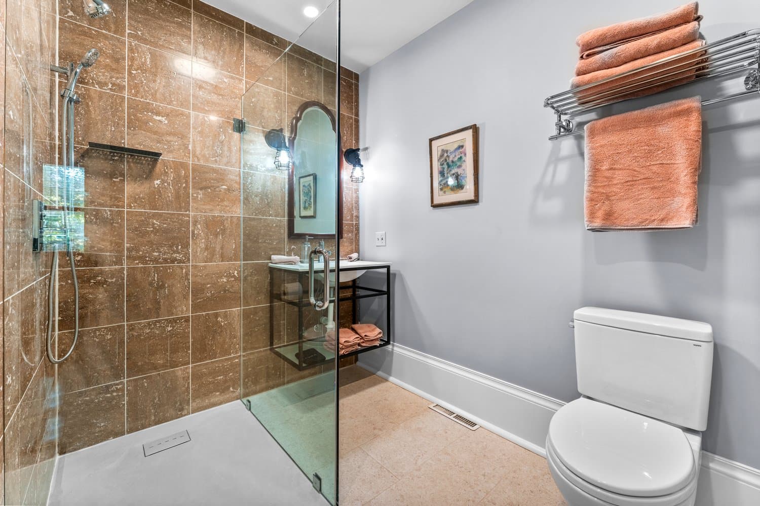 Gleaming bathroom with large glass-enclosed shower, wall-mounted sink, and toilet with towel rack overhead.