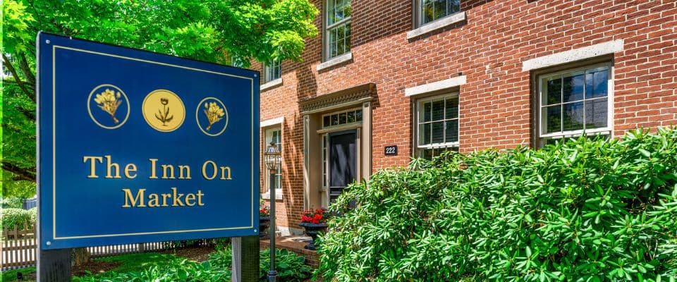 Sign for "The Inn On Market" in front of a brick building with greenery.