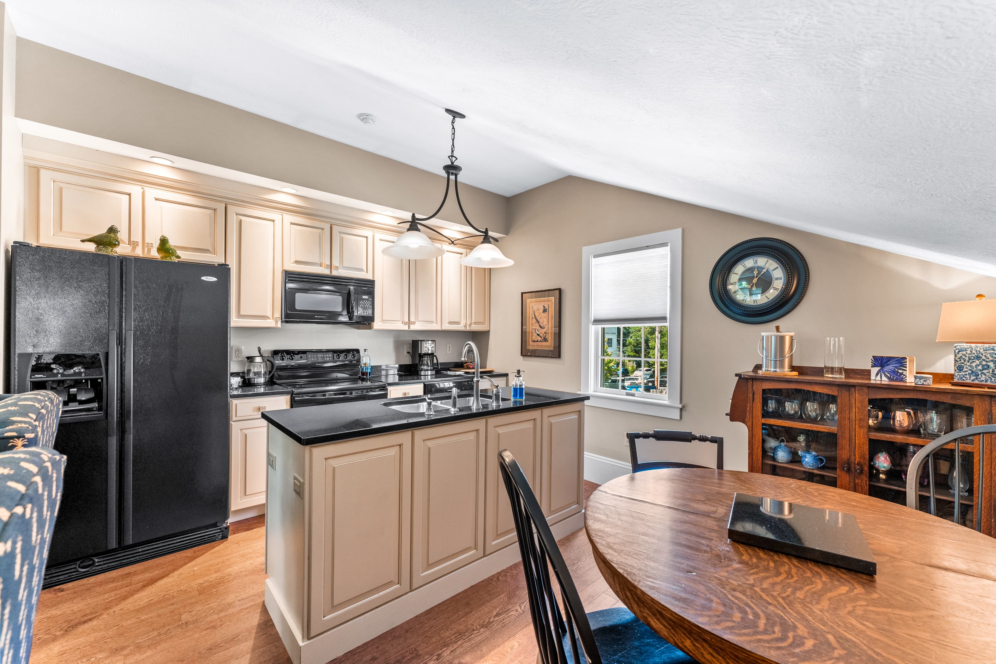 Modern kitchen with beige cabinetry, black appliances, and wooden dining table.