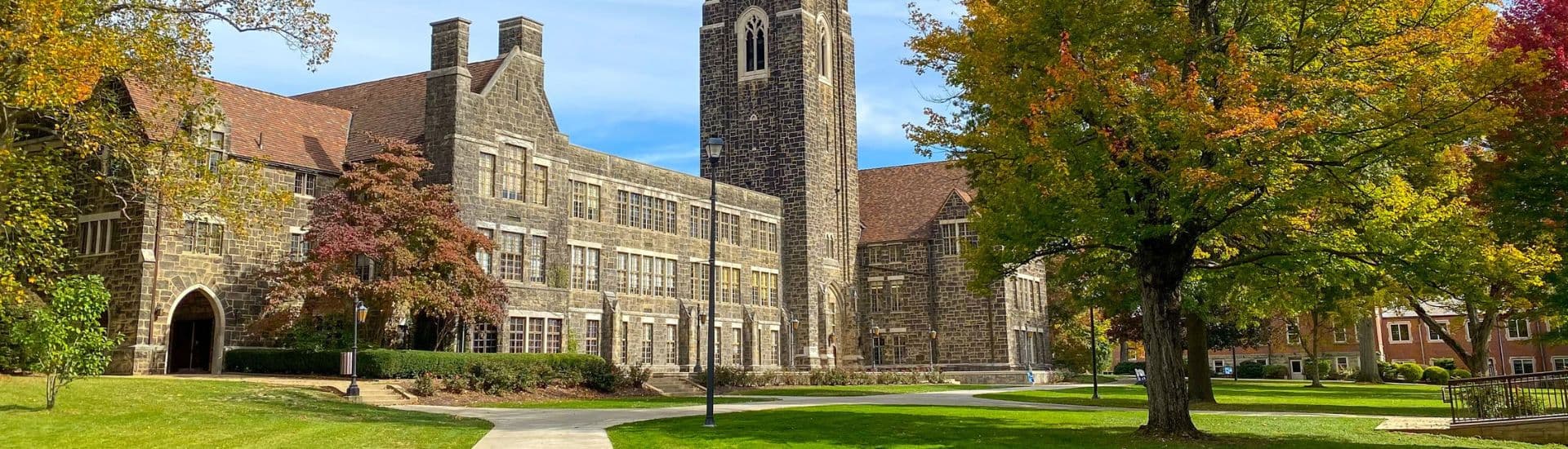 A stone building with a clock tower surrounded by colorful trees on a sunny day.