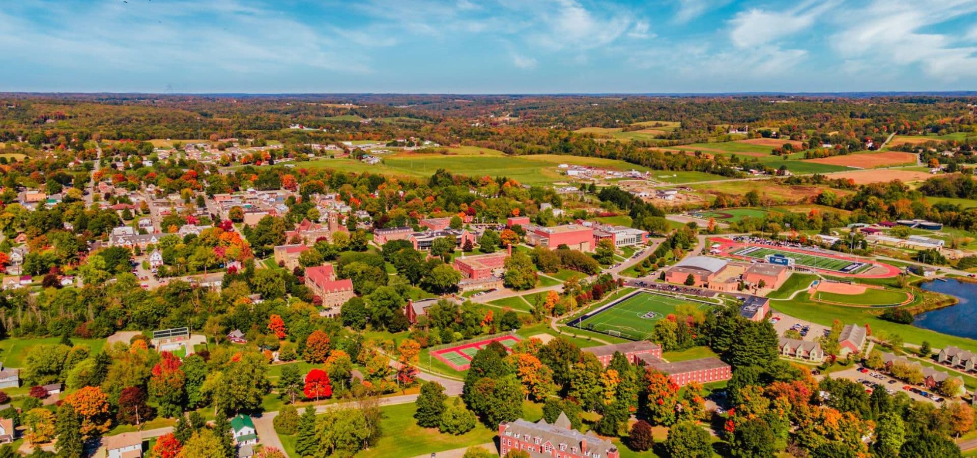 Aerial view of a college campus surrounded by colorful autumn foliage and nearby town.