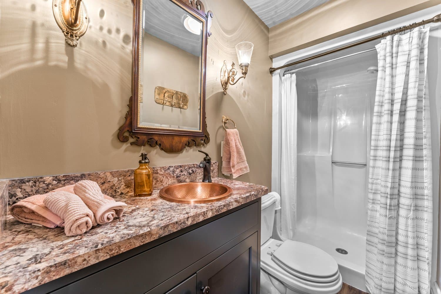 Compact bathroom with step-in shower, toilet, and vanity with copper sink.