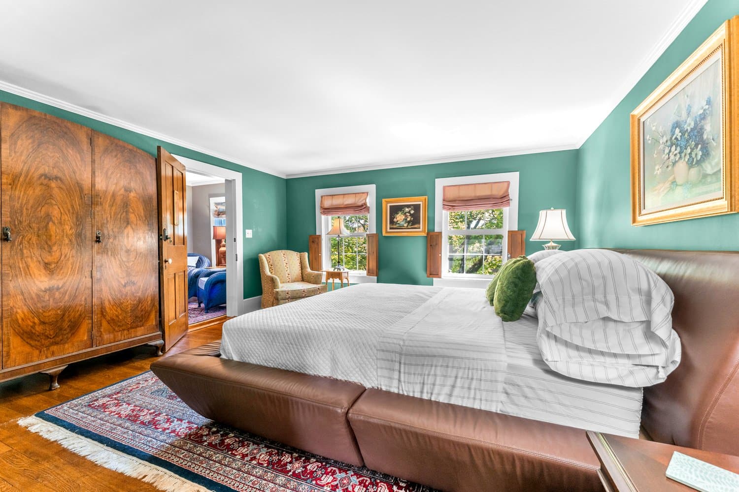 An inviting bedroom with king-size leather bed, upholstered armchair, hardwood floors, and an area rug.