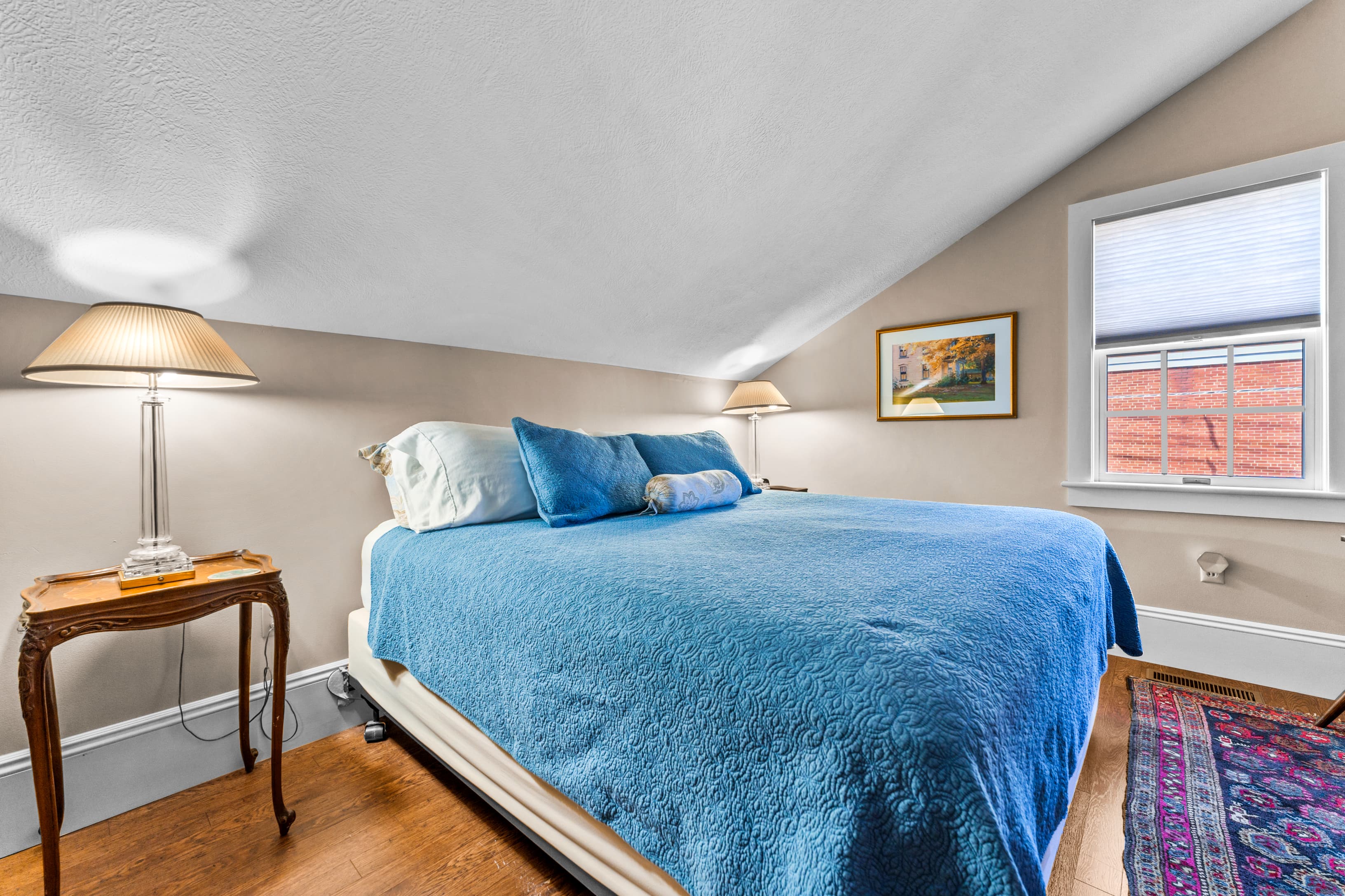 Cozy bedroom with a blue bedspread, a nightstand, and a window letting in natural light.