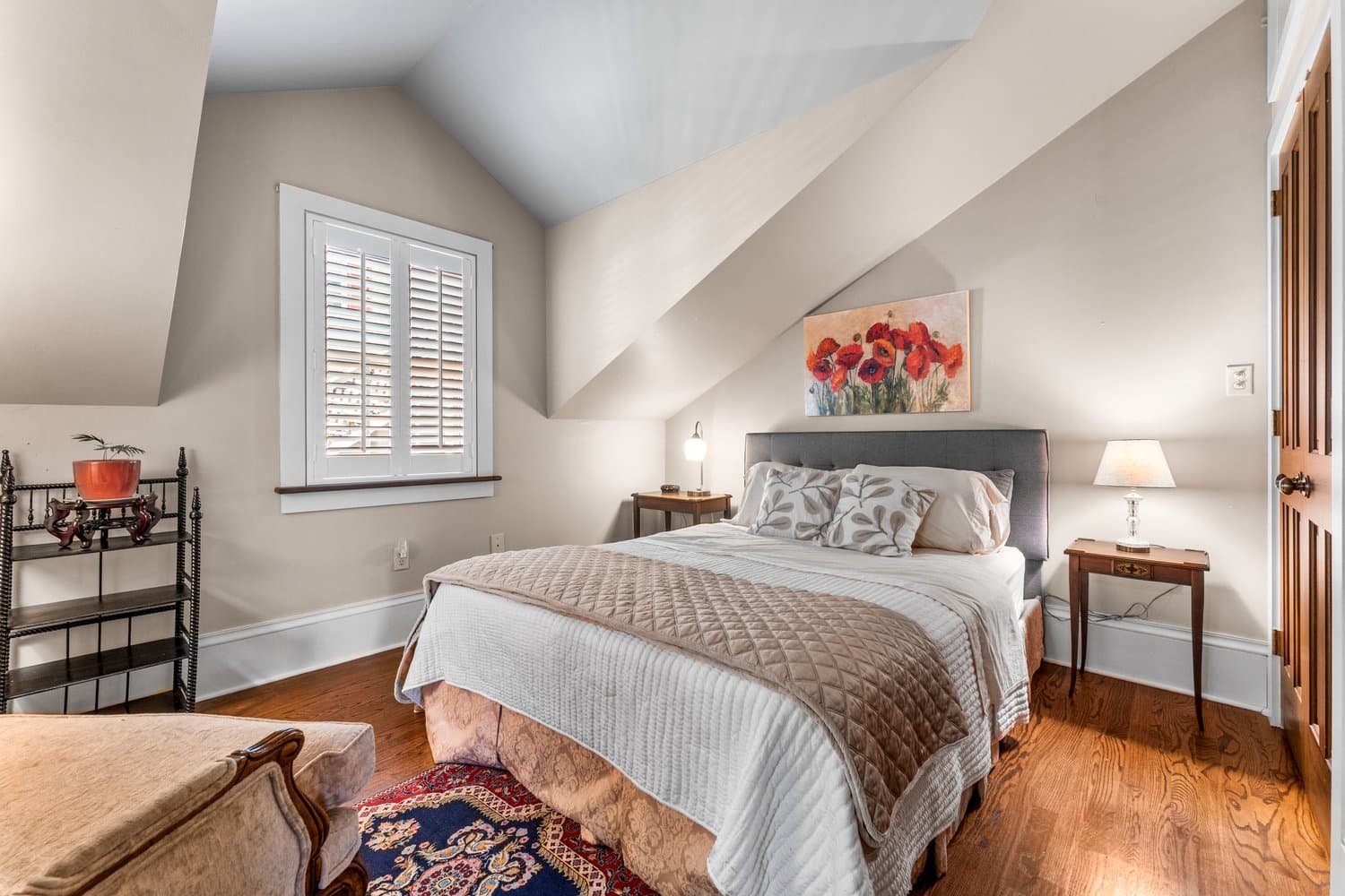 Charming bedroom with a cozy queen bed, sloped ceilings, hardwood floors, and soft lighting.