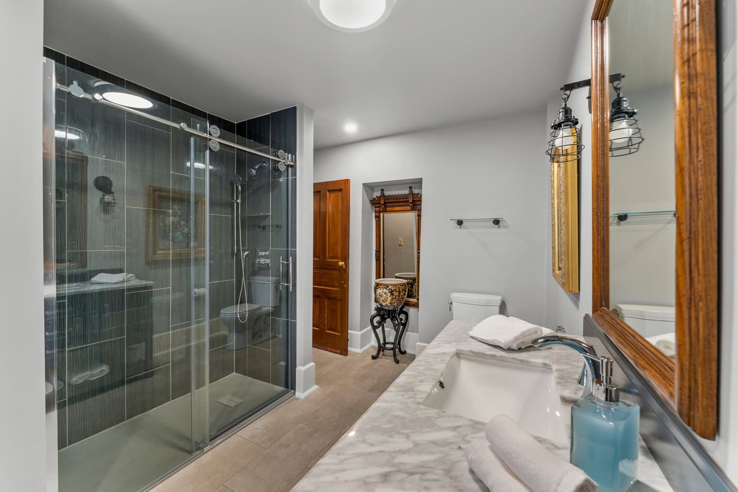Gorgeous bathroom with large glass-enclosed tiled shower, toilet, and sink with vanity.