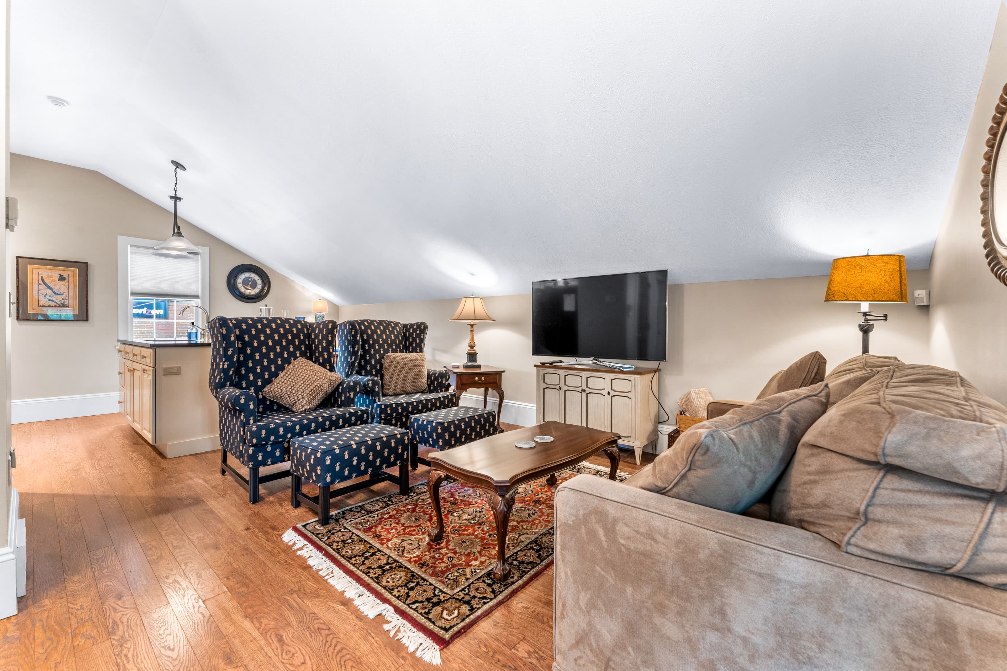 Cozy attic living room featuring two patterned chairs, a sofa, and a television.