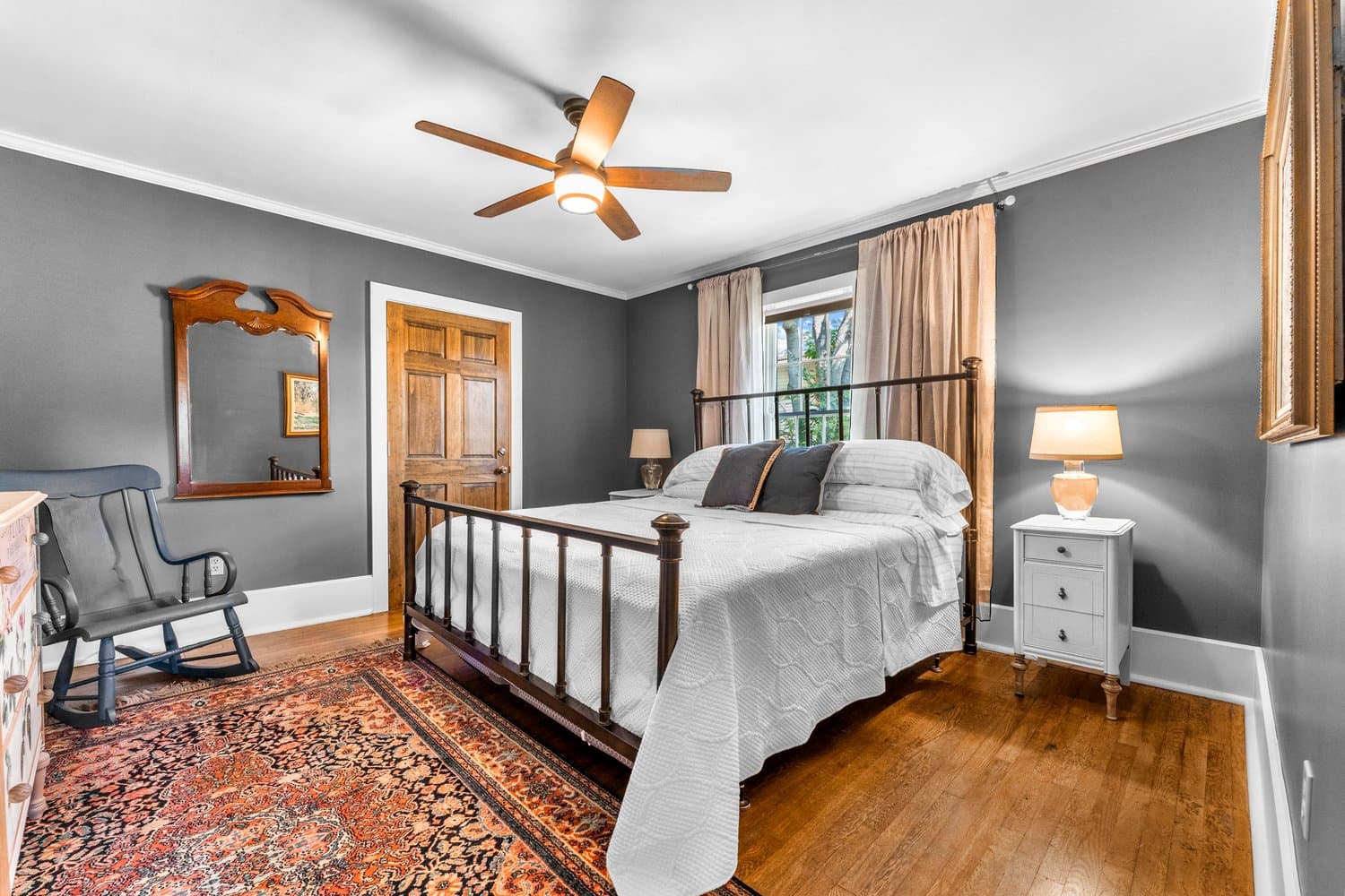 Well-lit bedroom with metal-framed king bed, hardwood floor, and ceiling fan.